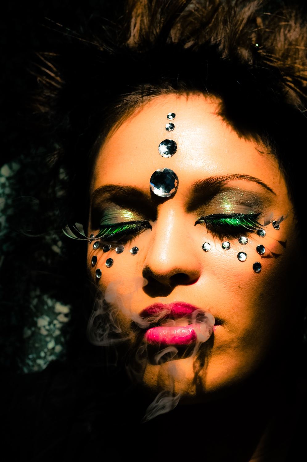 Close-up with crystals and green feather lashes, exhaling smoke