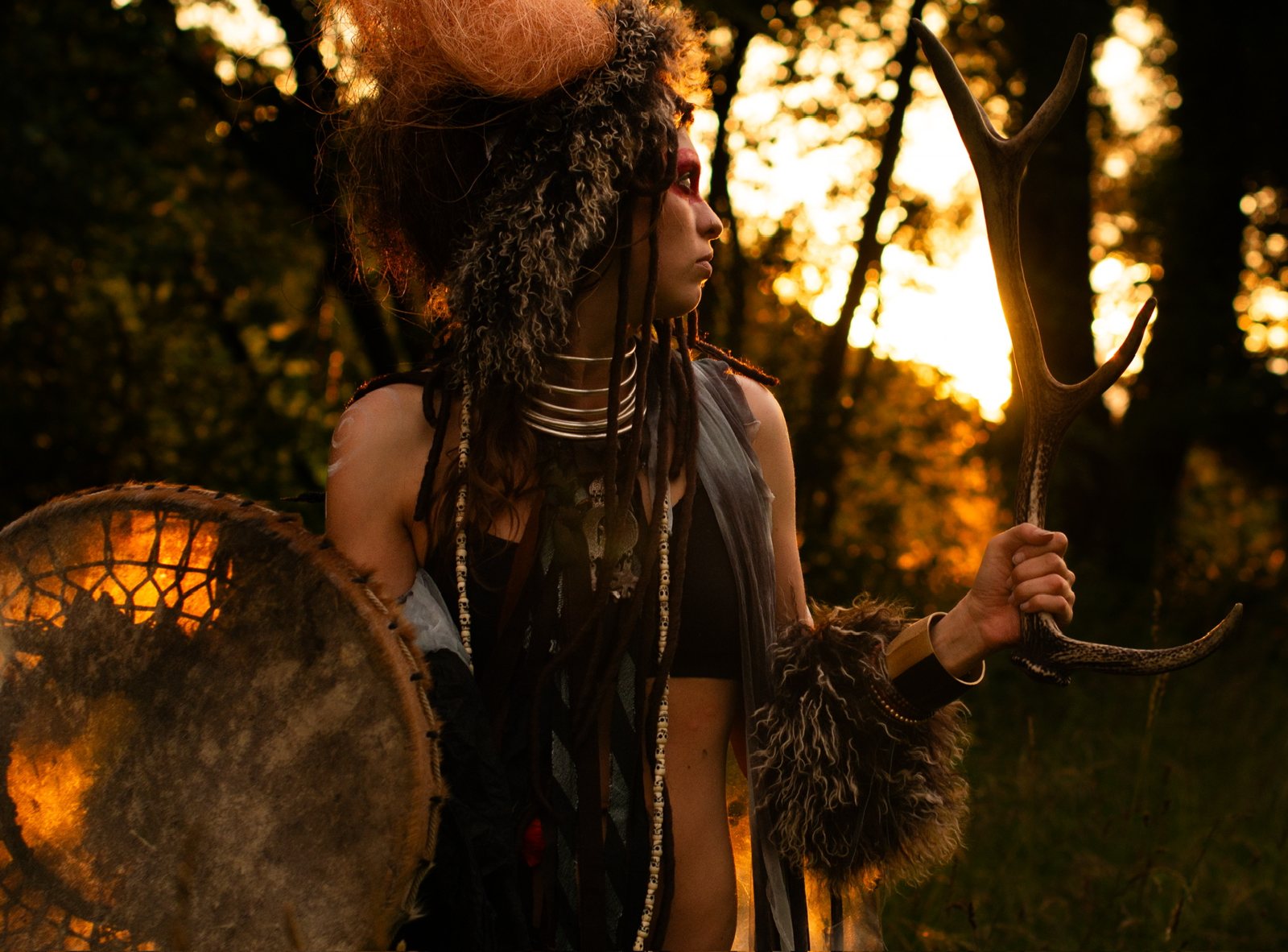 Shaman woman with drum and antler at sunset